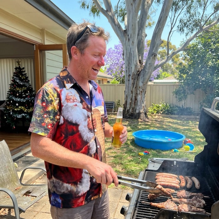 Man in a 3D Christmas print shirt at a backyard barbecue with tongs and a beer