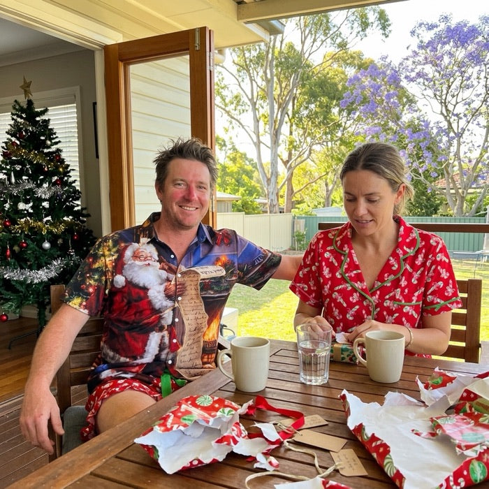 Couple on a sunny veranda on Christmas morning, he in a festive shirt and she in candy cane pyjamas