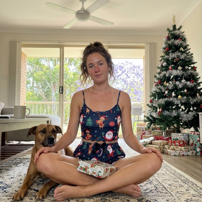 Woman in a Christmas cami pyjama set sitting by the tree with a gift on Christmas morning