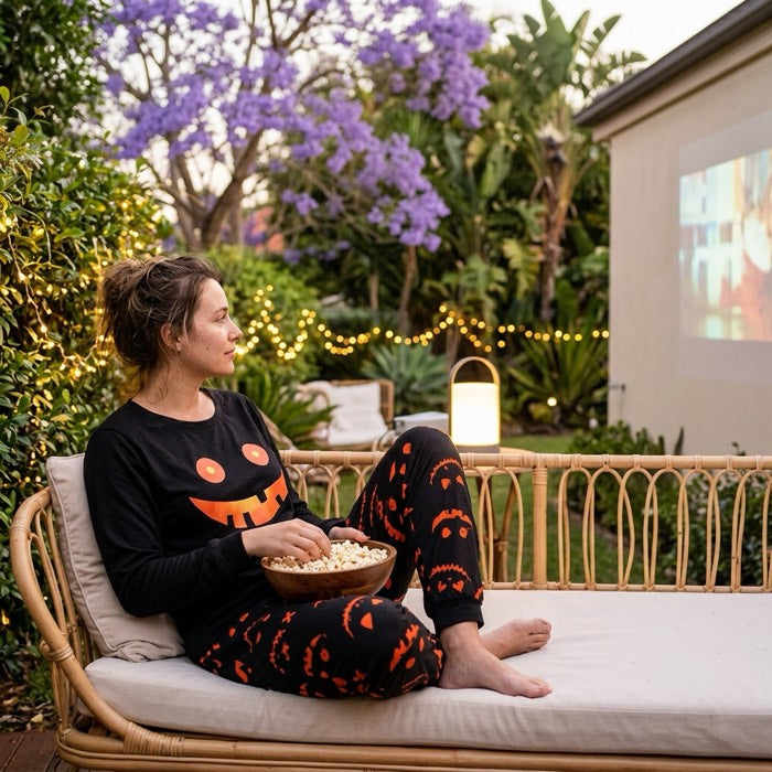 Woman in black pumpkin face pyjamas on an outdoor daybed watching a film