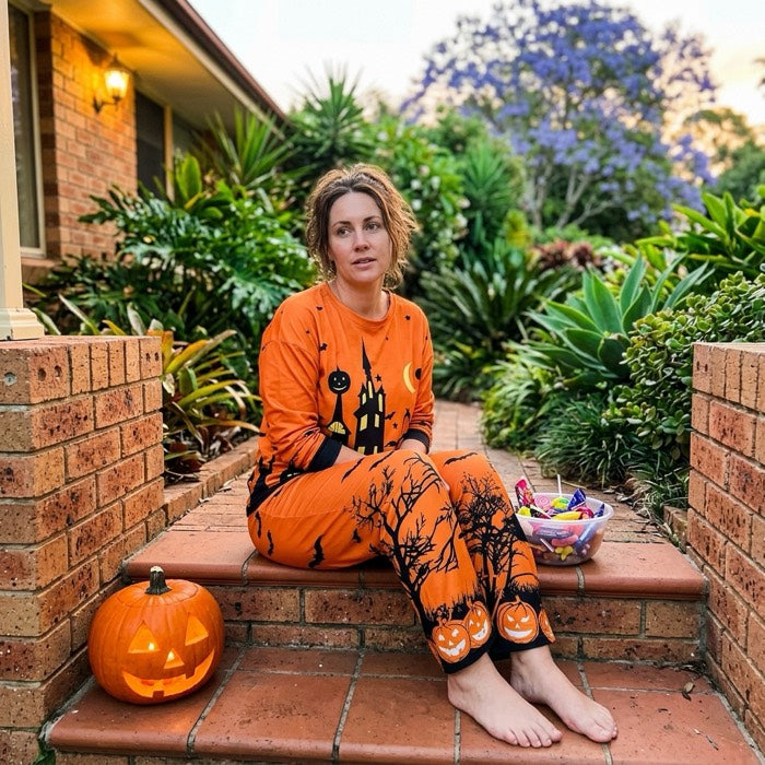 Woman in orange haunted house pyjamas on the front steps handing out lollies